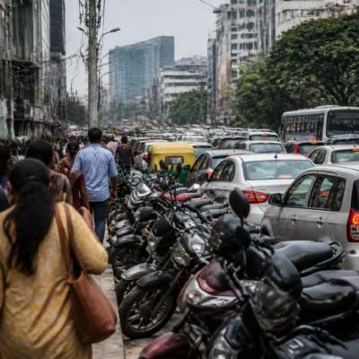Roadside vehicles parked along a busy Bengaluru street amid traffic and urban buildings