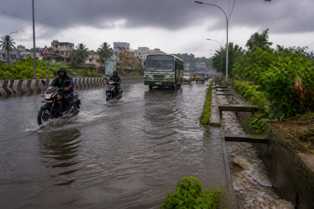 Tamil Nadu rain alert over a flooded urban road with commuters and dark monsoon clouds