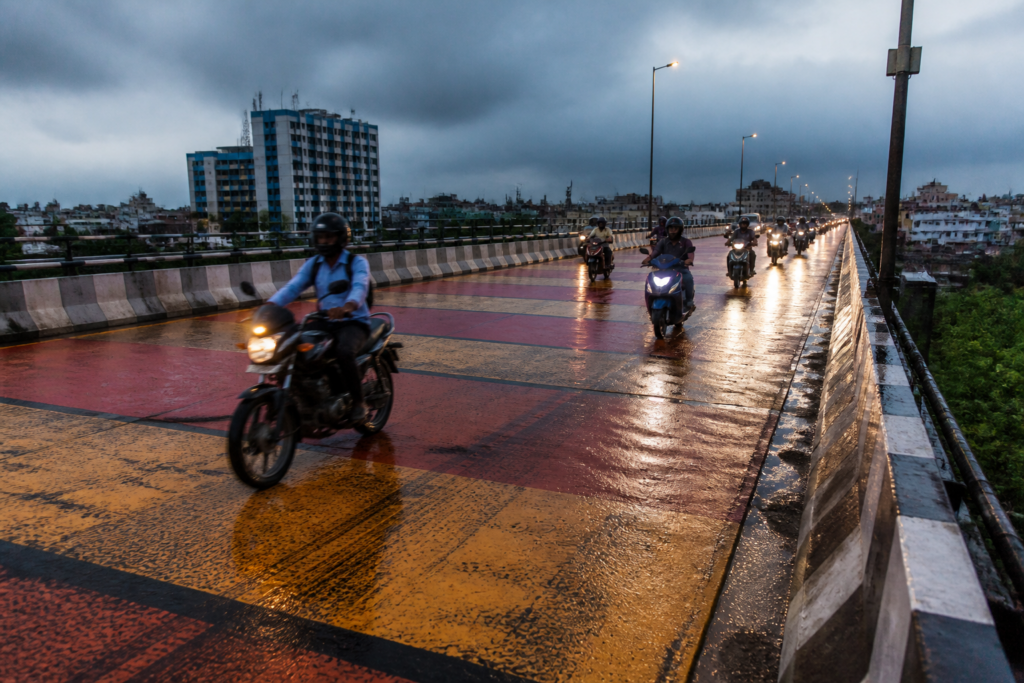 Rain-wet Chingrighata flyover with motorcycles on a coloured road surface in Kolkata