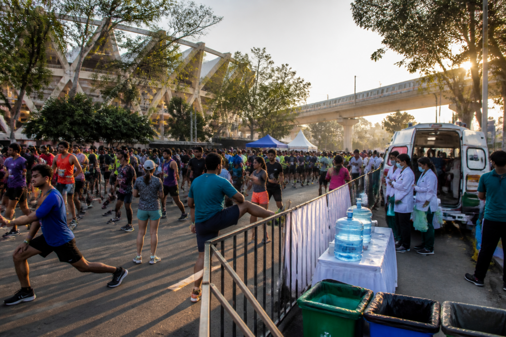 Delhi Half Marathon runners preparing near Jawaharlal Nehru Stadium with city infrastructure behind them