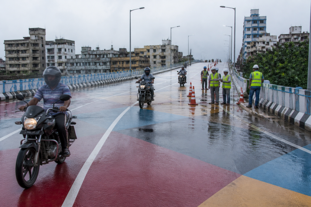 Kolkata painted flyover wet after rain, with motorcycles and road-safety activity