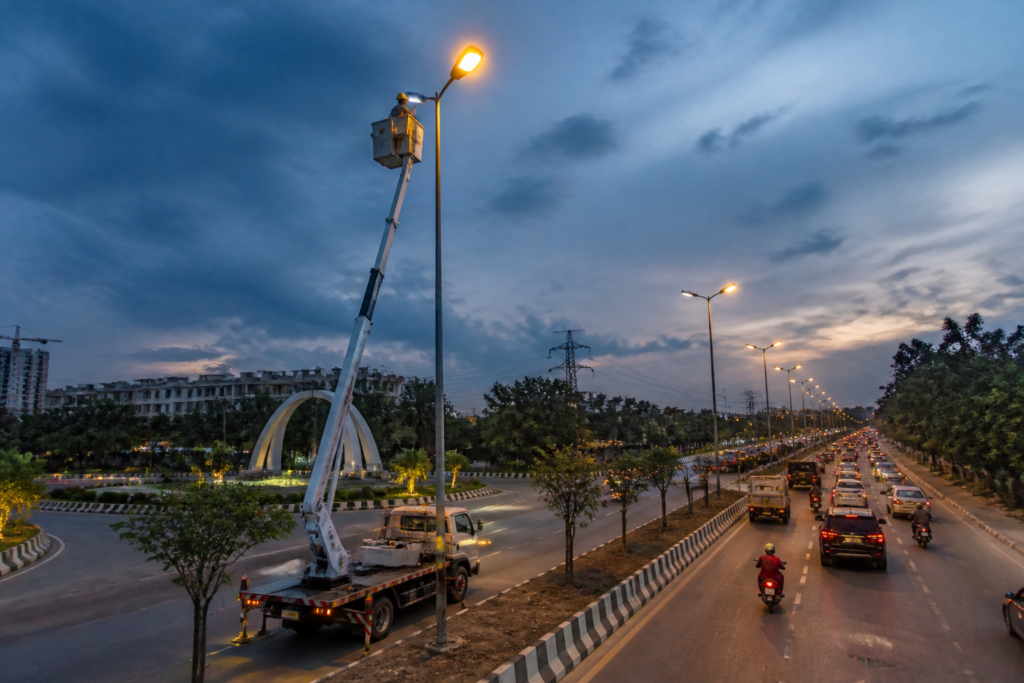 Greater Noida street lights being installed along a road near residential sectors and village settlements