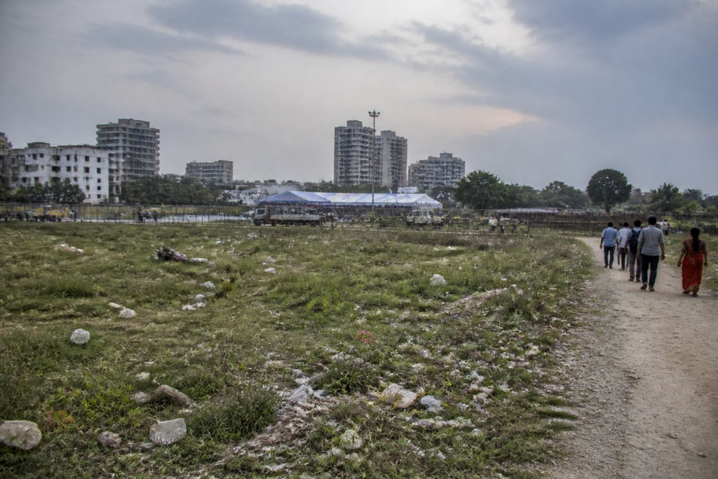 Delhi protest sites at a poorly maintained public ground with overgrown grass and waste