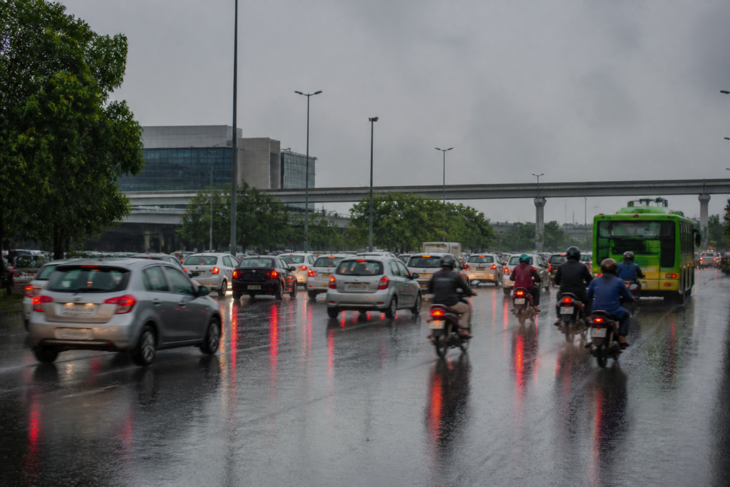 Delhi rain falling over a city road with wet streets and traffic under a grey sky