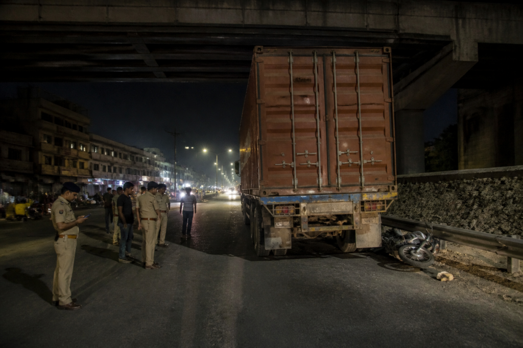 Ahmedabad container crash site near Sanathal railway bridge with a parked truck and damaged motorcycle.