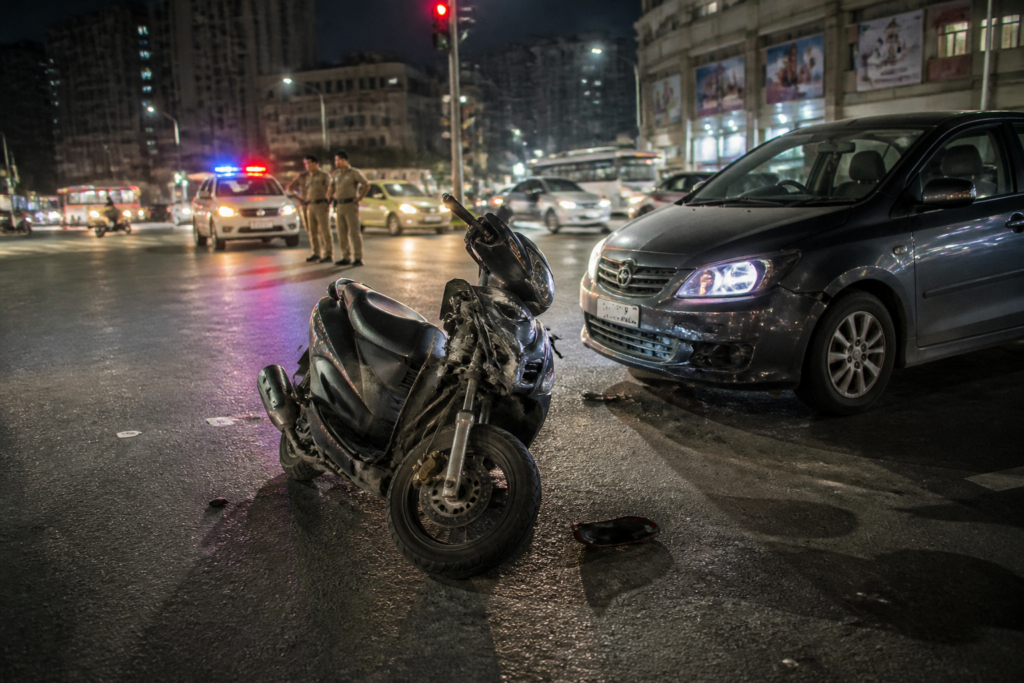 Ahmedabad Drive-In Road accident scene with a car and damaged moped near a city junction