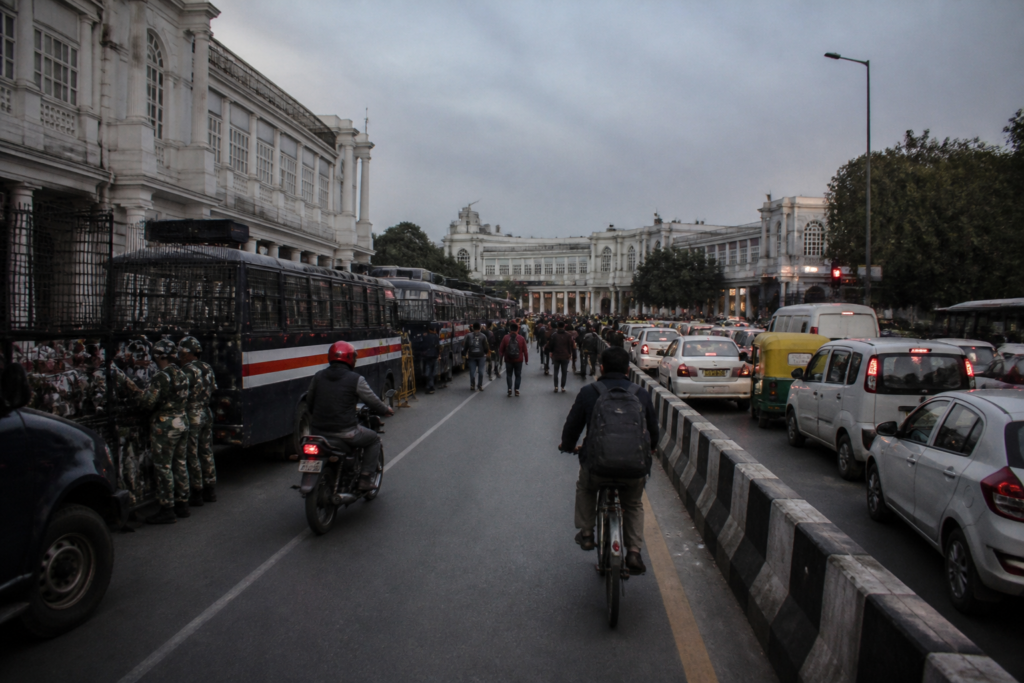 Central Delhi traffic restrictions near Connaught Place during a protest, with police vehicles and commuters on the road.