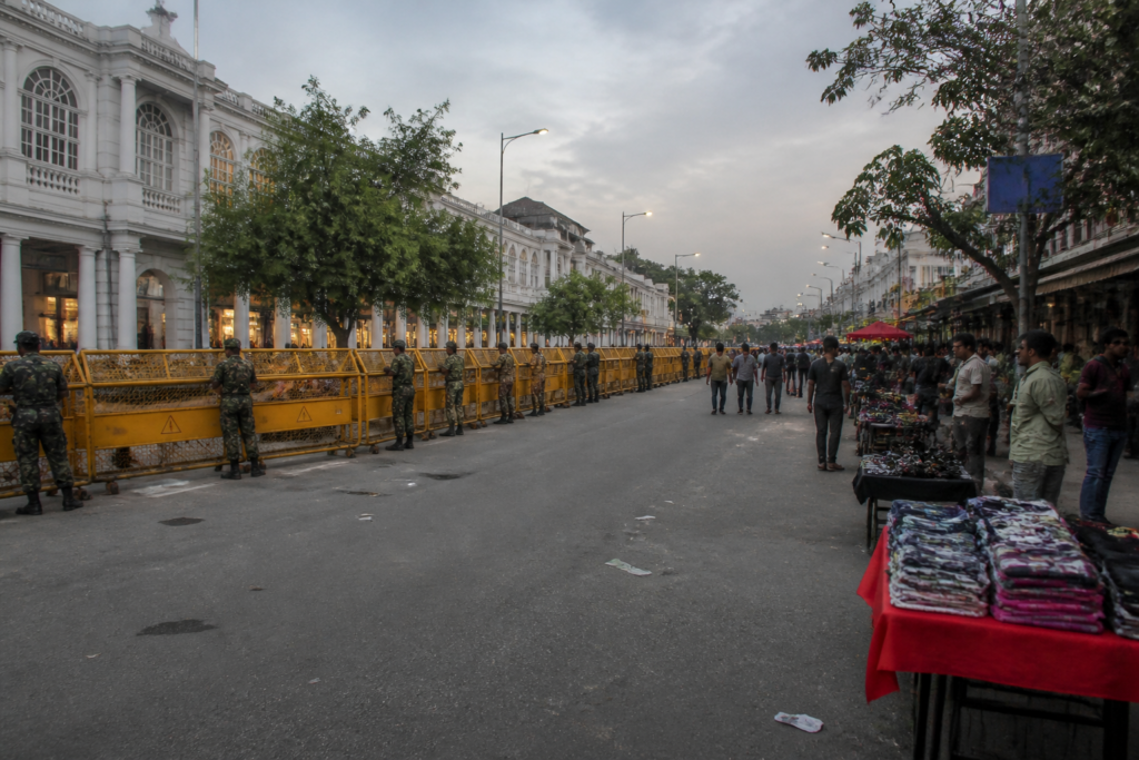Central Delhi protests behind barricades near Connaught Place, with commercial streets and vendors affected.