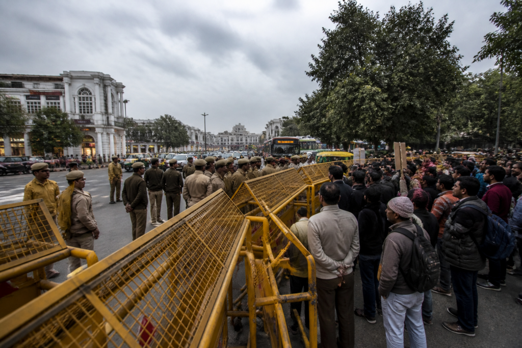 Delhi protest detentions near a central Delhi road with police barricades and detained protesters