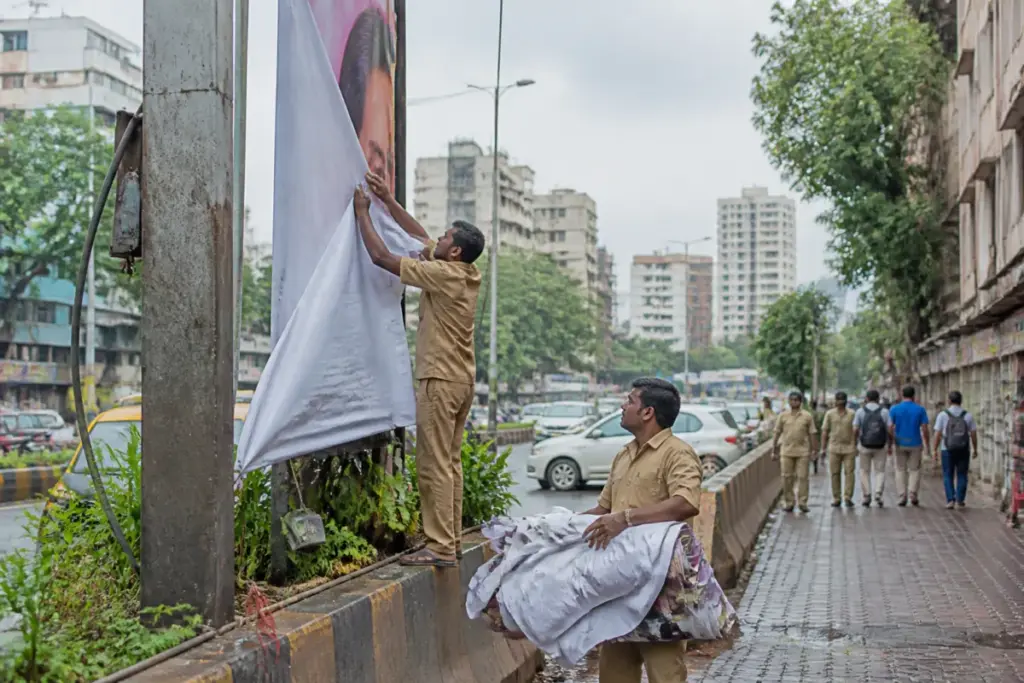 BMC workers remove illegal banners in Mumbai from a public road and building frontage.
