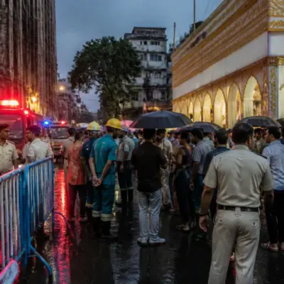 Kolkata pandal stampede site with crowds, barricades and emergency responders in a rain-soaked street