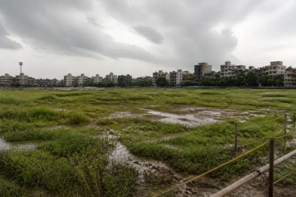 Delhi protest sites at CBD Ground, showing an open field with tall grass and muddy patches
