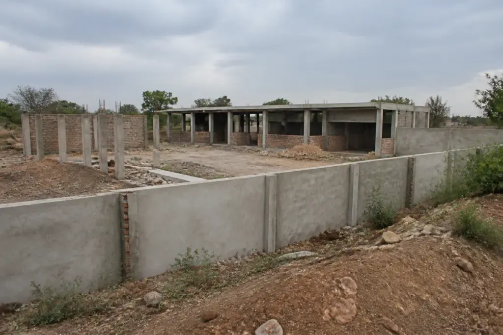 Incomplete Rewa cowshed project with a partly built boundary wall