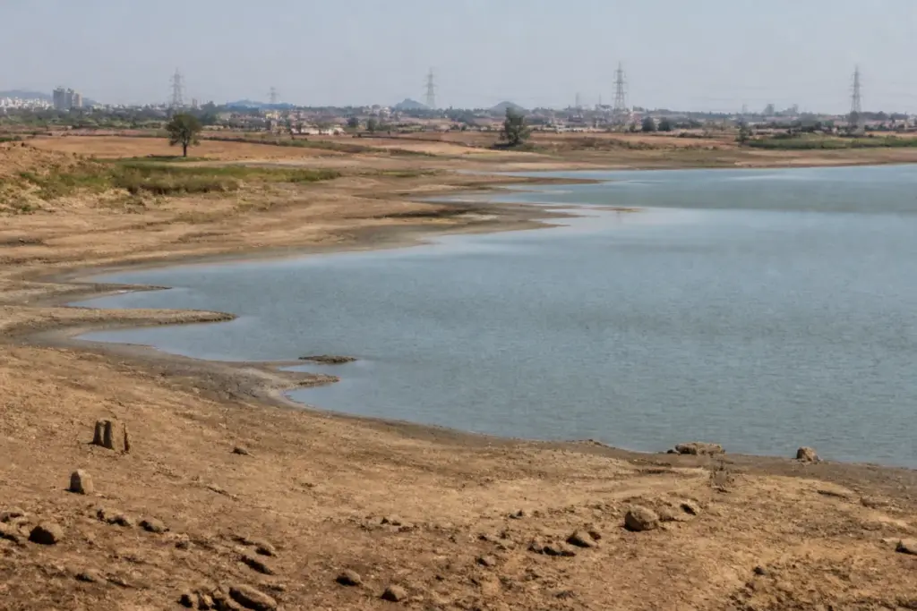 India weak monsoon leaves a low-water reservoir and dry agricultural landscape under a hot sky